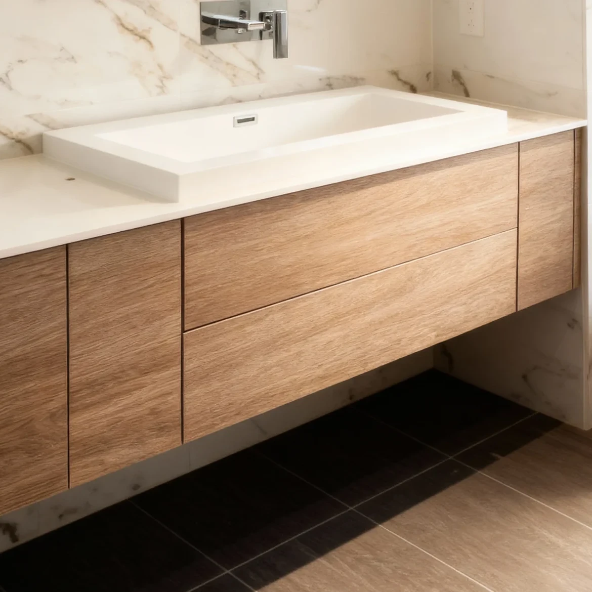 Komandor custom bathroom cabinetry featuring a wall-mounted floating vanity constructed from high-density European thermal-fused laminate in a natural wood tone. This bespoke millwork utilizes millimeter-precise manufacturing to ensure seamless architectural integration, featuring slab-style drawer fronts with a clean, hardware-free aesthetic. The integrated furniture system supports a large-format white trough sink and countertop, showcasing Komandor's ability to maximize space beauty and function through durable, locally manufactured custom interior solutions designed for modern Greater Toronto Area homes.