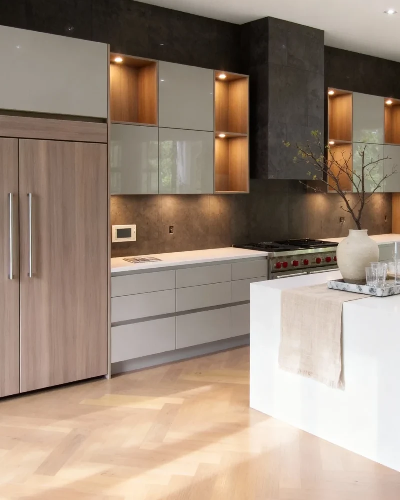 Komandor custom kitchen cabinetry featuring a frameless cabinet box construction and overlay cabinet door installation. The system includes high-gloss slab style door and drawer fronts paired with textured European laminate panels. This high-end architectural furniture system integrates recessed LED lighting into horizontal shelving units, highlighting the precision-engineered 18mm thermal-fused laminate. The installation demonstrates Komandor’s millimetric customization for luxury residential spaces, utilizing under-mount soft-close full-extension drawer slides and designer hardware.