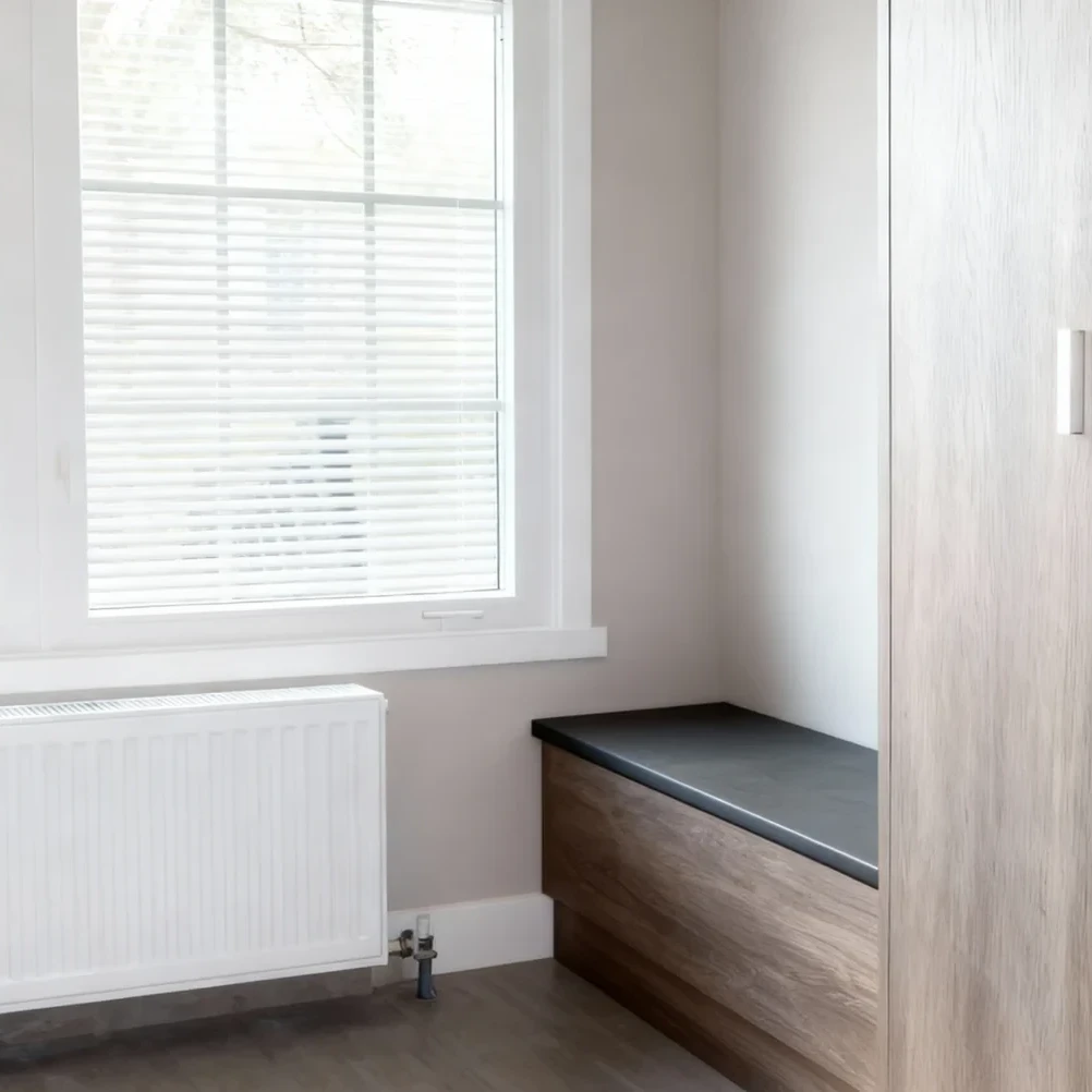 Komandor custom mudroom storage solution featuring a low-profile seating bench constructed from high-density 18mm European thermal-fused laminate in a natural wood-grain texture. The bench is integrated with a solid core slab vertical gable and features a charcoal black top surface. The cabinetry utilizes millimeter-precise manufacturing to ensure a seamless architectural fit against the wall, providing a durable, moisture-resistant storage foundation for residential entryway applications.
