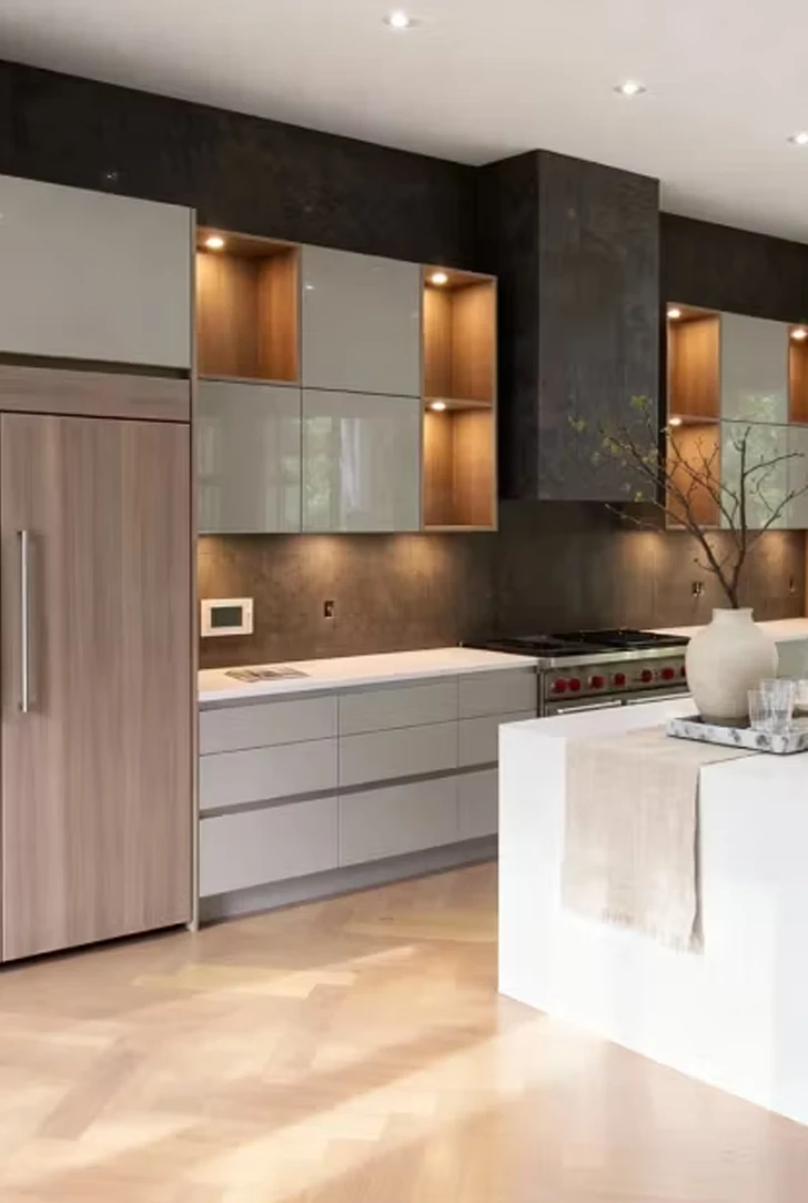 Komandor GTA custom luxury kitchen featuring a modern hybrid architectural design with two-tone cabinetry. The layout showcases high-gloss light grey upper cabinets contrasted by warm natural wood vertical storage units with integrated recessed LED lighting, a signature of Komandor’s technical precision. A central white quartz waterfall island anchors the space, complemented by a charcoal black stone backsplash and light oak herringbone flooring. The floor-to-ceiling millwork demonstrates Canadian-made craftsmanship optimized for space maximization and seamless appliance integration in a high-end Greater Toronto Area home.