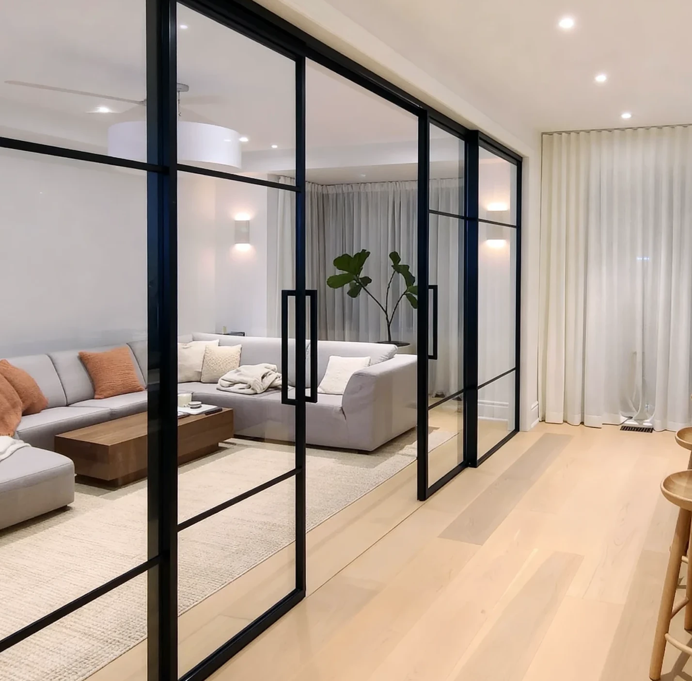 Komandor Lumi aluminum-framed interior glazing system and glass wall partition featuring a matte black finish. This high-end architectural partition utilizes an aluminum framed interior glazing system with a swing door and fixed panels. The Lumi system provides a stylish solution to divide open space while maintaining transparency. The structural framework is engineered with precision aluminum profiles that accept various insert materials, providing a modern, minimalist aesthetic for residential interiors and custom room divisions.