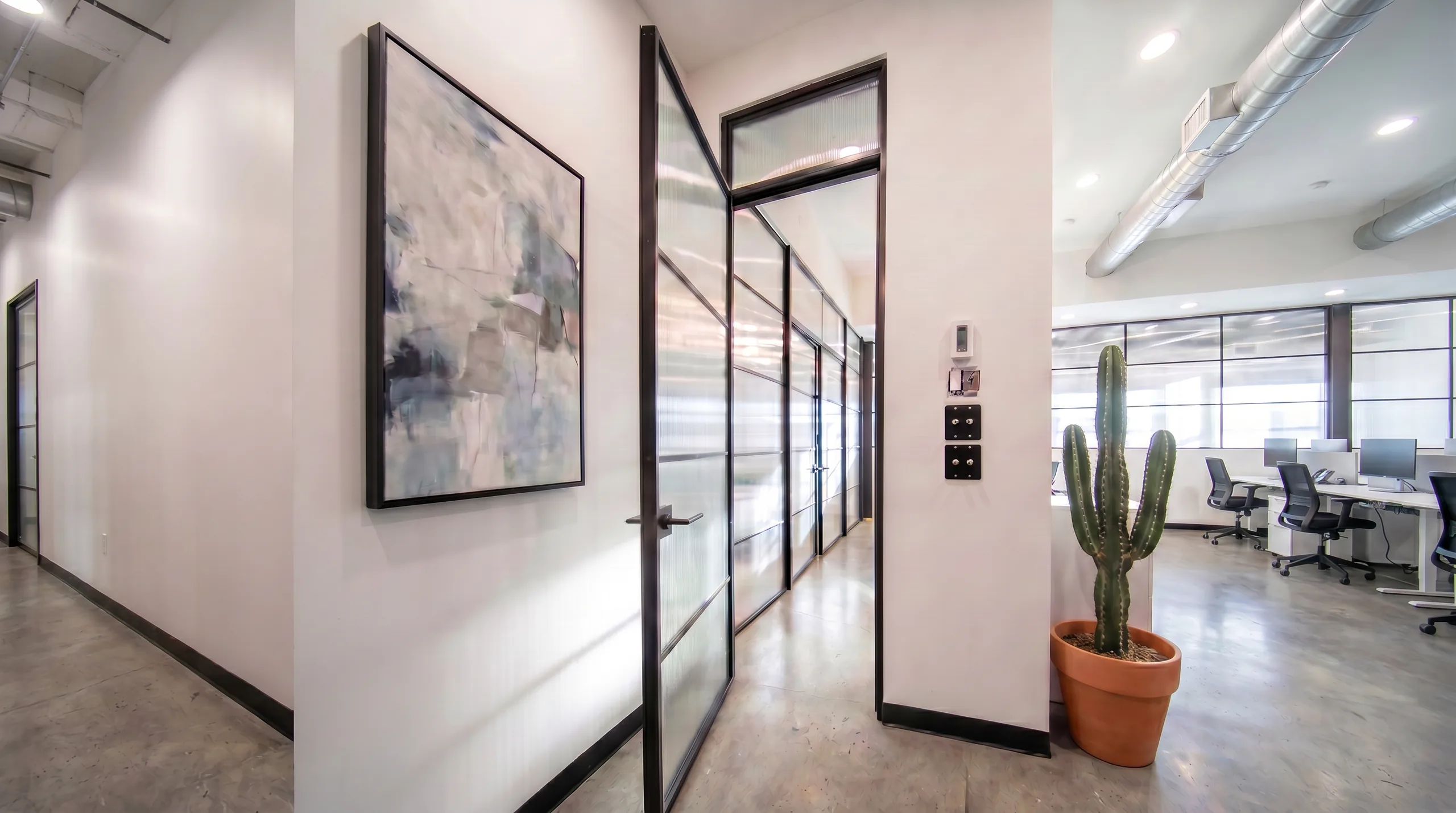 Fluted glass office partition set in slim black aluminum frames lining a corridor by Komandor
